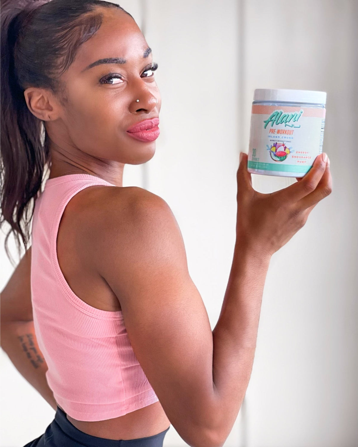 A woman in a pink top holding a container of Pre-Workout in Island Crush flavor.