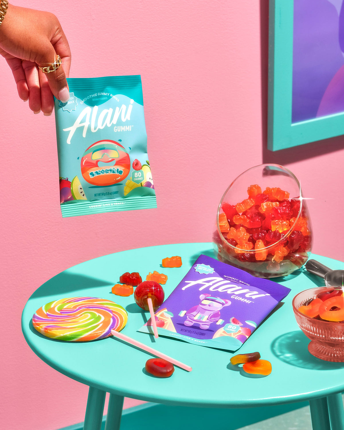 A women holding up a Gummi in Smoothie Gummy Rings flavor next to a blue table with candy. 